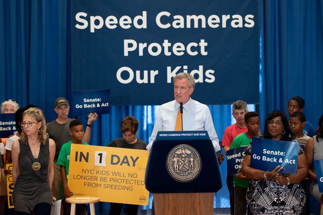 Mayor de Blasio with supporters in front of a sign that says "Speed Cameras save lives"